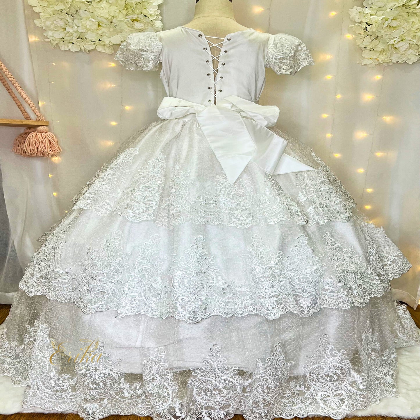 Back view of a white tiered Communion dress featuring a large satin bow and corset back