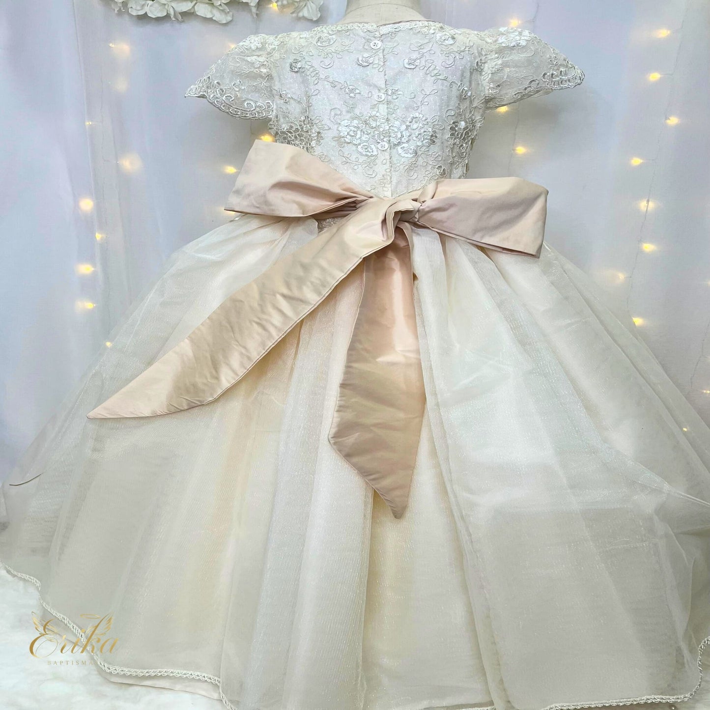 Back view of a pearl communion dress featuring a large satin bow and button-up lace bodice